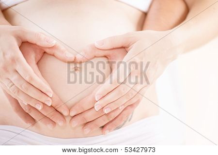 Pregnant Belly with fingers Heart symbol. Beautiful Young Pregnant Woman and Her Husband Together Caressing Her Pregnant Belly. Pregnancy. Love Concept. Mom and Dad waiting for newborn baby. Parents 