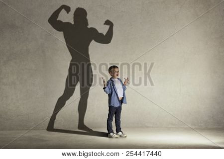 The Little Boy Dreaming About Athletic Bodybuilder Figure With Muscles. Childhood And Dream Concept.