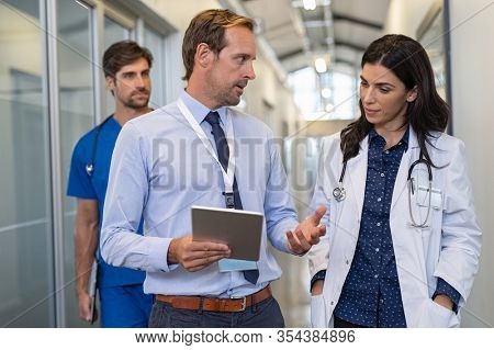 Man and woman doctor having a discussion in hospital hallway. Doctor discussing patient case status with his medical staff after operation. Pharmaceutical representative showing medical report.