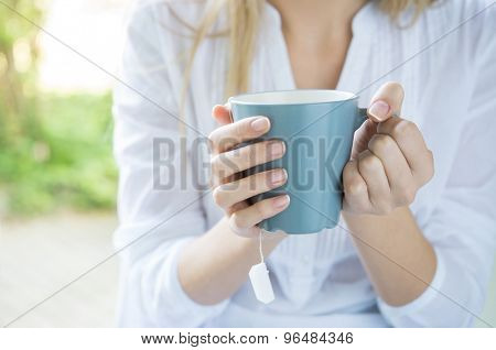 Closeup shot of a woman holding tea mug. Close up of young woman's hand holding a cup of hot tea. Relaxed girl drinking tea. Shallow depth of field with focus on tea mug.
