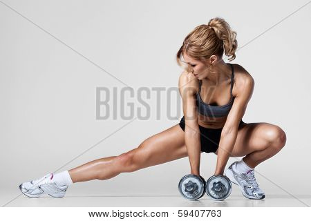 Smiling athletic woman pumping up muscles with dumbbells and stretching legs