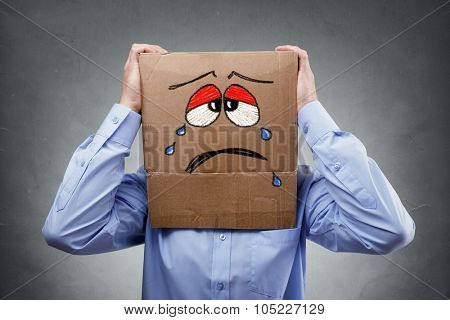 Businessman with cardboard box on his head showing a crying sad expression concept for headache, depression, sadness, heartache or frustration