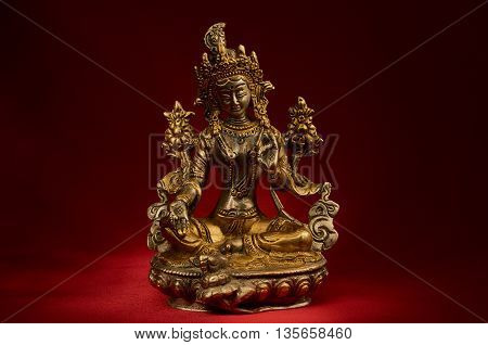 Statuette of Green Tara on a red background. Vajrayana deity quick to help and protection. Om tare tuttare ture soha.