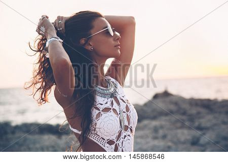 Beautiful boho styled girl wearing white crochet swimsuit with flash tattoo at the beach in sunlight