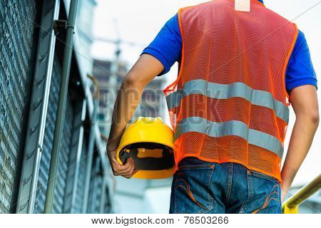 Asian Indonesian construction worker with helmet and safety vest on a building site in Asia