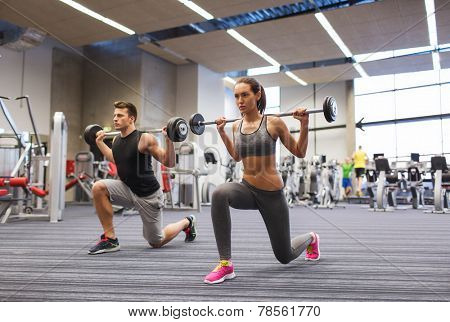 sport, bodybuilding, lifestyle and people concept - young man and woman with barbell flexing muscles and making shoulder press lunge in gym