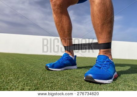 Resistance band workout man at fitness gym training calf muscles with rubber bands. Bodyweight exercises outdoor at park.