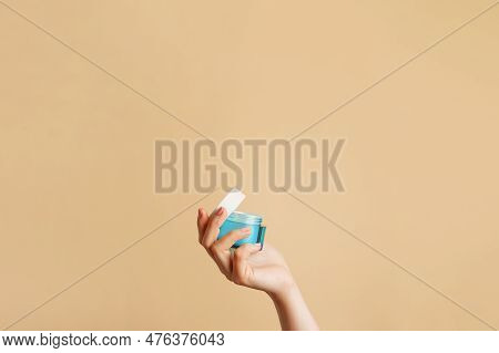 Woman Holding A Blue Glass Jar Of Skin Cream On Beige Background. Skin Care Concept. Moisturizing Cr