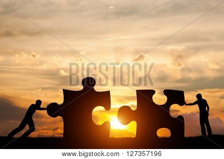 Two men connect two puzzle pieces. Sunset sky. Concept of business solution, teamwork, solving a problem, challenge