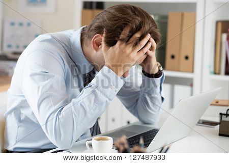 Tired business man at workplace in office holding his head in hands. Sleepy worker early in the morning after late night work. Overworking making mistake stress termination or depression concept