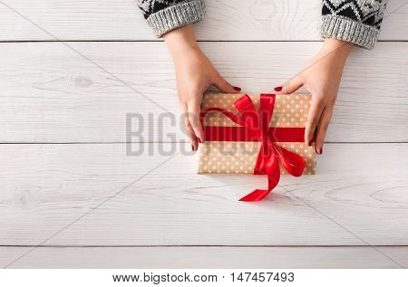 DIY hobby. Woman's hands wrapping christmas or other holiday handmade present in paper with red ribbon. Give present box, decoration of gift on white wooden table, top view with copy space