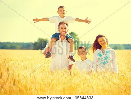 Happy Young Family with two children walking on wheat summer field. Healthy mother, father and little sons enjoying nature together, outdoors. Healthy Smiling Dad, Mom and kids together. Harvest