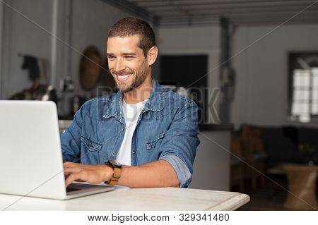 Happy young businessman using laptop at home. Young man working on computer at home. Casual entrepreneur feeling excited about new project while working on laptop at home.