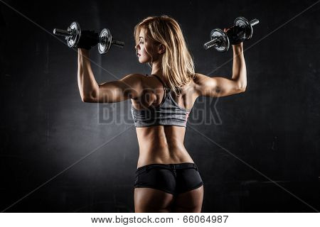 Brutal athletic woman pumping up muscles with dumbbells