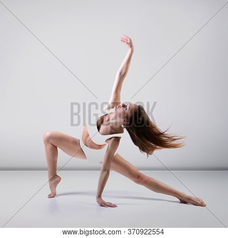 Dance. Young beautiful graceful woman with perfect slim sporty body dancing and jumping at studio over gray background. Female beautiful contemporary dance. Ease of movement, youth, grace