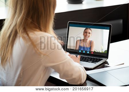 Two young women chatting online by making video call on laptop, using videoconferencing app for communication with distance friend, studying online course, virtual learning, close up rear view