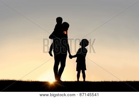 Silhouette Of Mother And Young Children Holding Hands At Sunset