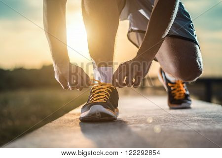 Man tying jogging shoes.A person running outdoors on a sunny day. The person is wearing black running shoes.Focus on a side view of two human hands reaching down to a athletic shoe.