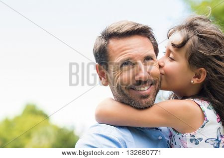 Portrait of a little girl kissing her dad on cheek. Pretty girl giving a kiss to her father outdoor. Loving child embrace and kissing her father.