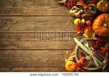 Autumn background from fallen leaves and fruits with vintage place setting on old wooden table. Thanksgiving day concept