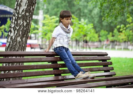 Stylish little boy sitting on a bench in a summer park