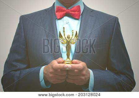 Awards ceremony. Business success. Best worker. The winner man holds in front of him the Golden statuette in his hands.