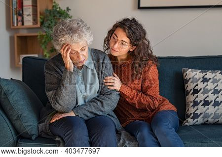 Caring daughter comforting frustrated unhappy senior woman. Loving adult granddaughter talking to sad old grandmother and comforting her. Upset widowed woman with headache consoled by her daughter.