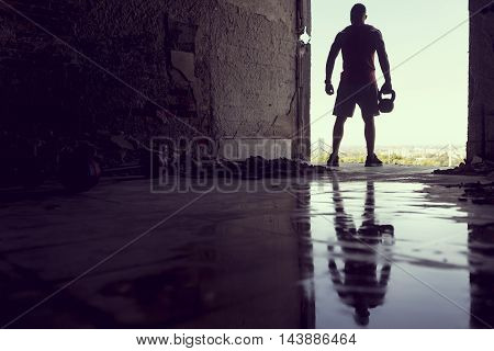 Muscular athletic built young athlete working out in a ruin building next to a puddle of water.  training with barbells and kettlebell deadlifting