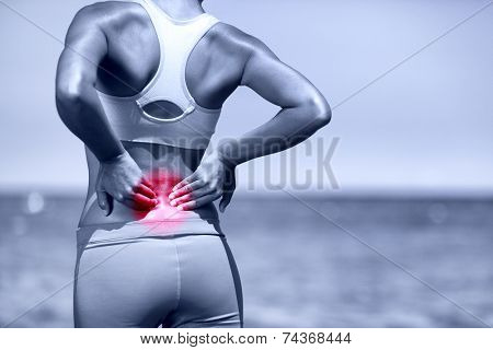 Back pain. Athletic running woman with back injury in sportswear rubbing touching lower back muscles standing on road outside.