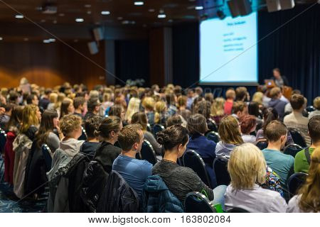 Business and entrepreneurship symposium. Speaker giving a talk at business meeting. Audience in the conference hall. Rear view of unrecognized participant in audience.