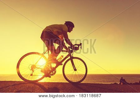 Road bike cyclist man cycling. Biking Sports fitness athlete riding bike on an open road to the sunset. Cyclist biking on road bike with sun flare. Active healthy sports lifestyle athlete cycling.