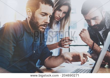 Business team concept.Young professionals discussing new business project in modern office.Group of three people analyze reports on laptop computer.Horizontal, blurred background.Flares