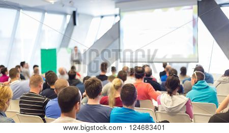 Man giving presentation in lecture hall. Male speeker having talk at public event. Participants listening to lecture. Rear view, focus on people in audience.