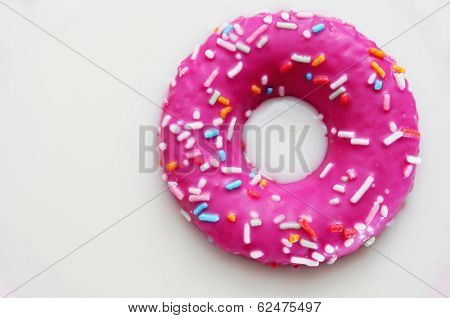 a donut coated with a pink frosting and sprinkles of different colors soaking in milk