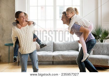 Laughing Parents Holding Kids On Back Giving Children Piggyback Ride Playing Together At Home, Cheer