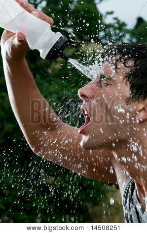 Young tired athlete splashing and pouring fresh water on his head to refresh during a running trail