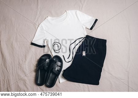 White T-shirt, Black Shorts, Black Slippers, Necklace And Nail Polish On Grey Background. Overhead V