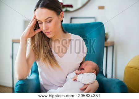 Stressed Mother Holding Crying Baby Suffering From Post Natal Depression At Home