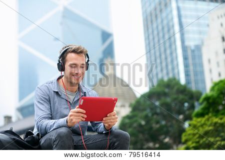 Man talking on tablet pc having video chat conversation in sitting outside using app on 4g wireless device wearing headphones. Casual young urban professional male in his late 20s. Hong Kong.