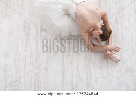 Beautiful graceful young ballerina in pointe shoes at white wooden floor background, top view from above with copy space. Ballet practice and stretching. Back of ballet dancer.