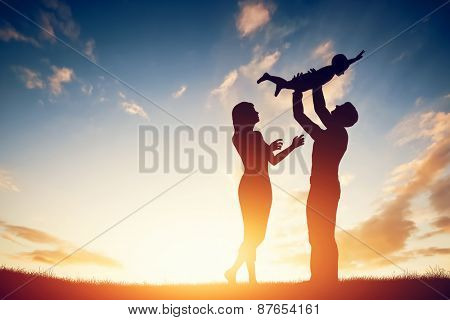 Happy family together, parents with their little child at sunset. Father raising baby up in the air.