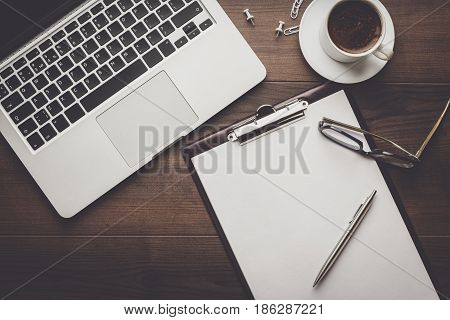 top view of an office table. brown wooden office desk with cup of coffee, notepad and laptop computer. working office space. office objects on the table. office working atmosphere