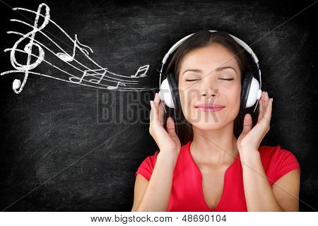 Music - woman wearing headphones listening to music with music notes drawn on black blackboard texture background. Serene relaxing beautiful young multiracial Asian Caucasian girl enjoying music.