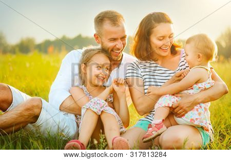 Happy joyful young family father, mother and little daughters having fun outdoors, playing together on a field. Mom, Dad and kids laughing and hugging, enjoying nature outside. Countryside