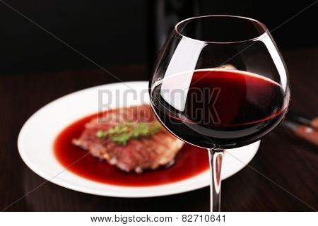 Glass of wine with grilled steak in wine sauce on dark background