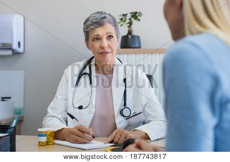 Senior female doctor listening to patient explaining her painful in her office. Mature woman doctor consulting patient in hospital room. Doctor and patient discussing health issue in office.