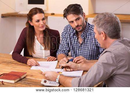 Businessman explaining loan policy to young couple. Happy young couple discussing with a financial agent their new investment. Financial consultant presents bank investments to a young couple. 
