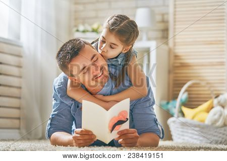 Happy father's day! Child daughter congratulating dad and giving him postcard. Daddy and girl smiling and hugging. Family holiday and togetherness.