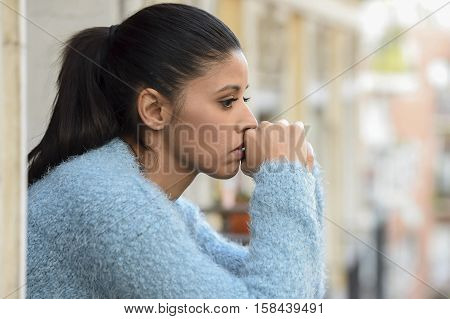 young beautiful sad and desperate hispanic woman suffering depression looking thoughtful and frustrated at apartment balcony looking depressed at the street