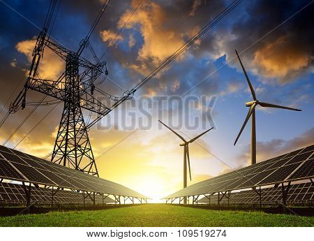 Solar panels with wind turbines and electricity pylon at sunset.